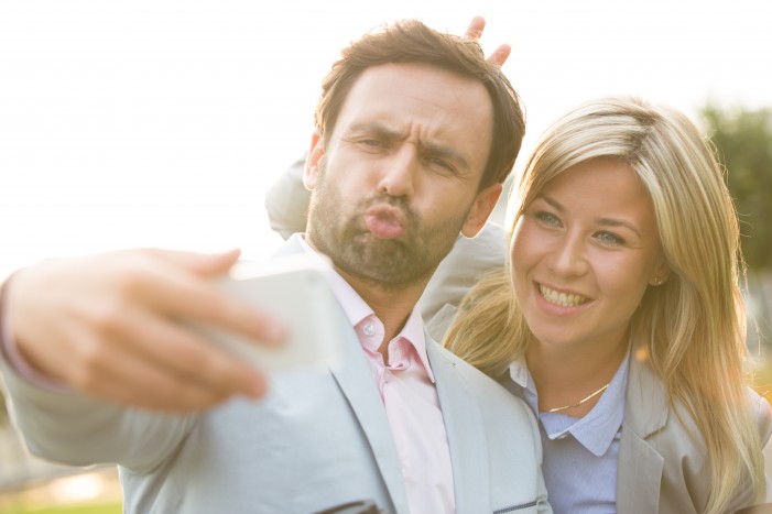 Playful business couple taking selfie outdoors on sunny day